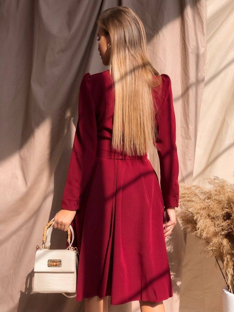 Woman in a red dress holding a white handbag against a textured wall.