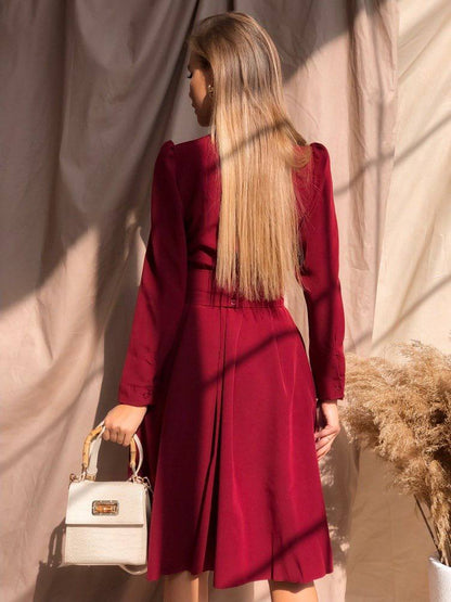 Woman in a red dress holding a white handbag against a textured wall.