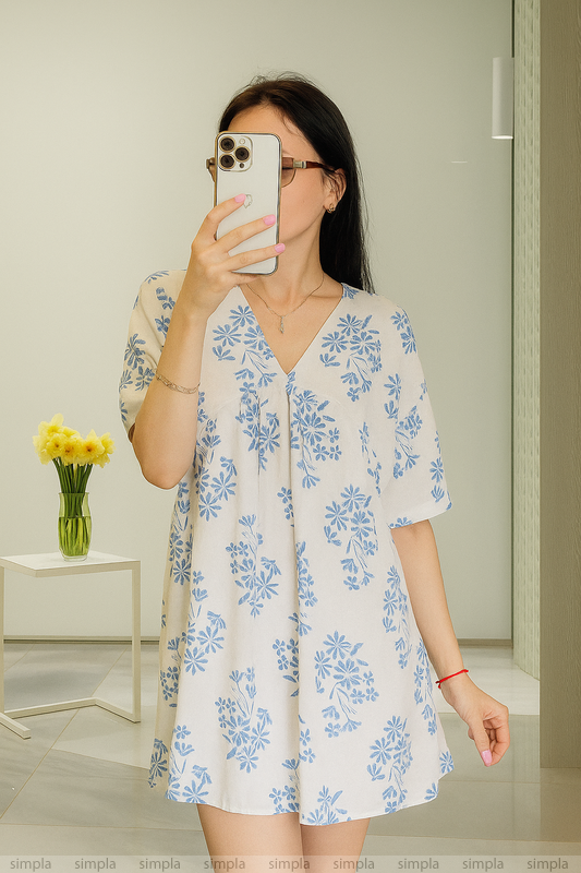 Woman taking a mirror selfie wearing a floral dress in a room.