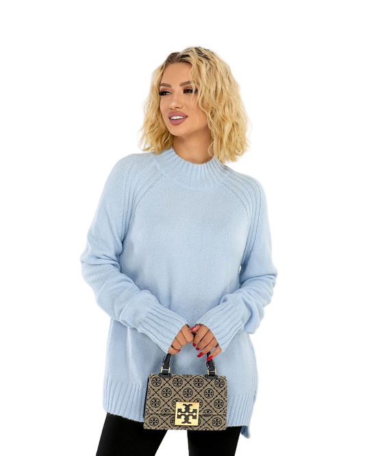 Woman wearing a light blue sweater holding a patterned handbag on a white background