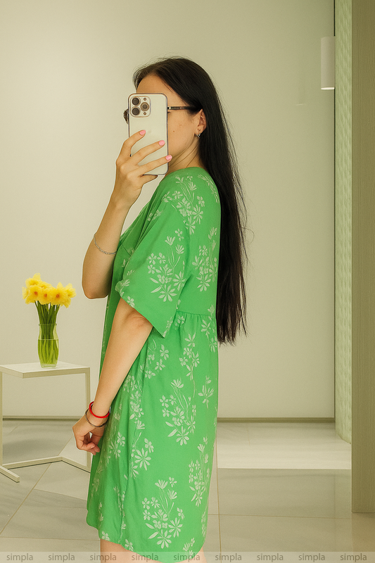 Woman in a green dress taking a mirror selfie in a minimalistic room.